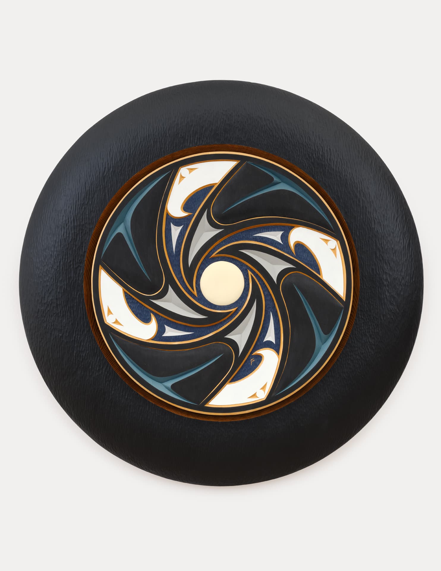 A circular decorative piece with a textured black outer ring. The inner design features a swirling pattern in shades of blue, gray, and white, with gold accents. A central white circle is surrounded by intertwining shapes that create a dynamic visual effect. The background is plain white.