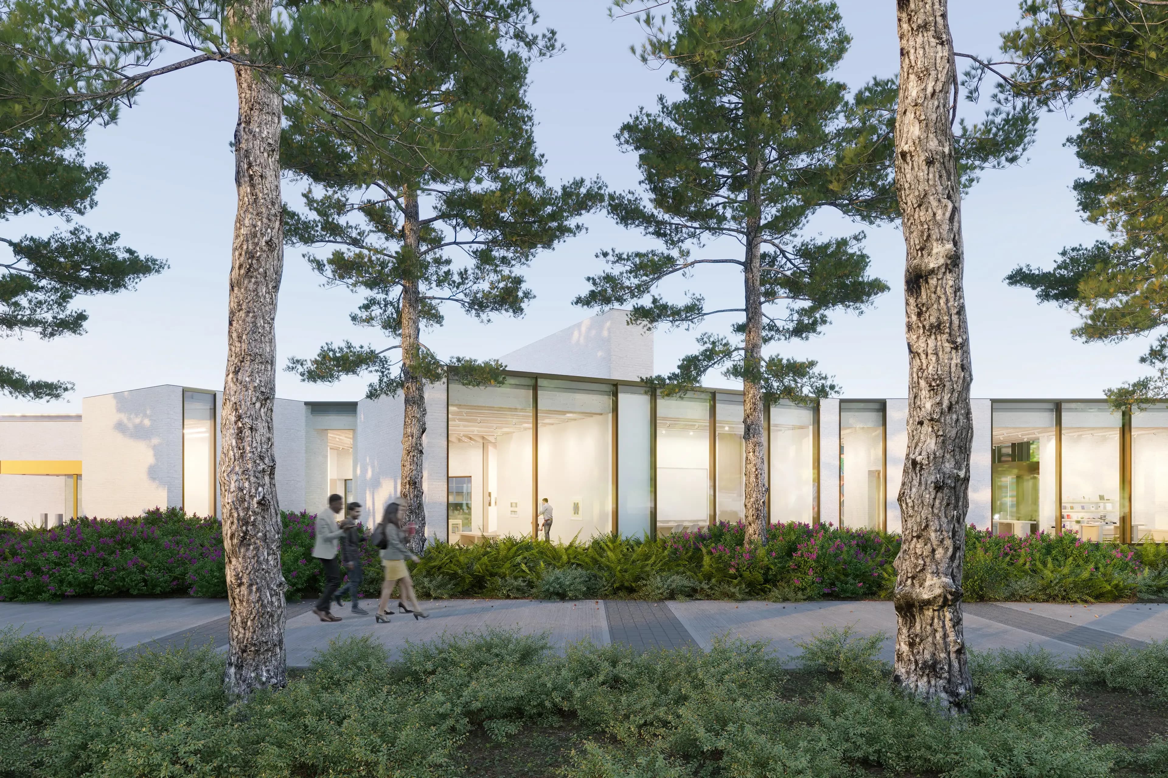 A contemporary building viewed through tall trees, featuring large glass windows and a modern design. Two people are walking on a pathway in the foreground, surrounded by lush greenery and colorful flowers. The setting suggests a serene outdoor environment.